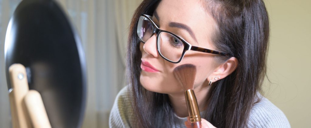 woman putting on makeup with eyeglasses
